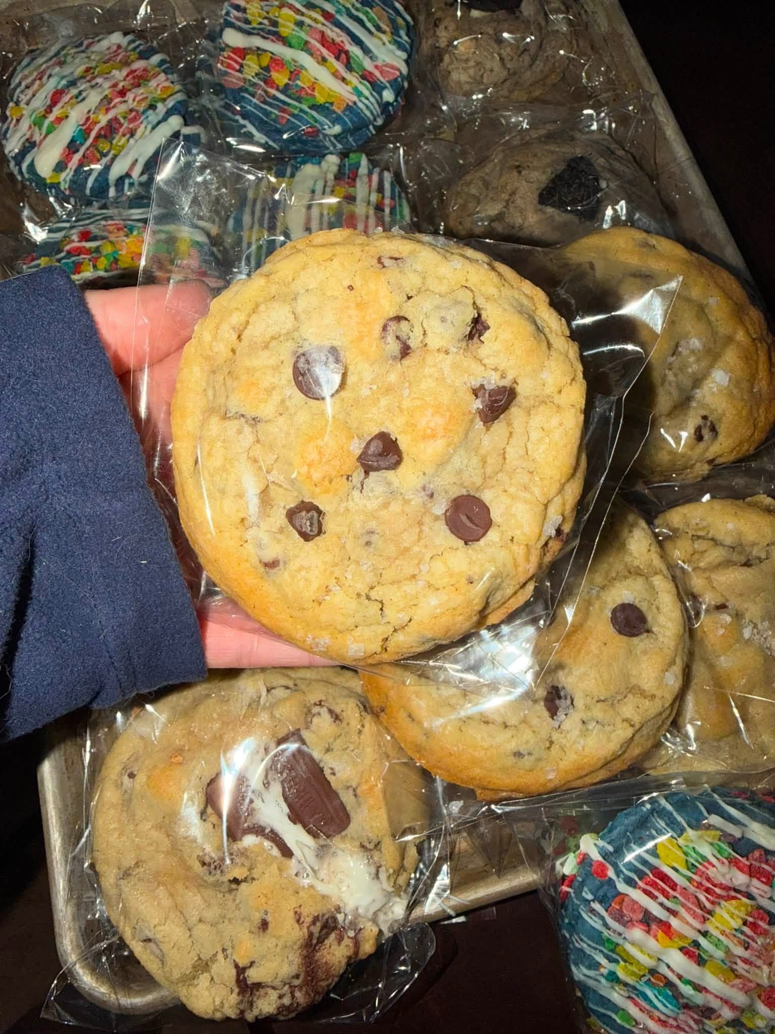 Sea salt chocolate chip cookie with a tray of assorted cookies behind it